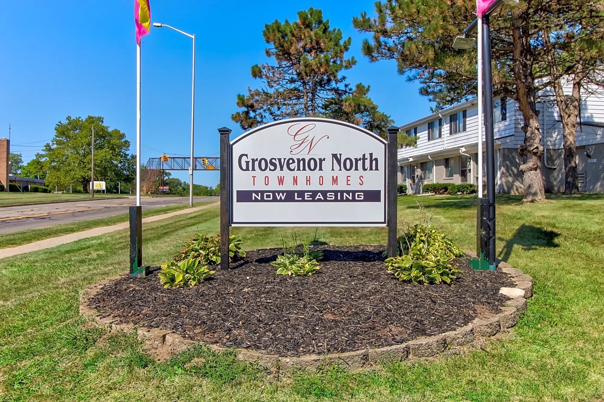 Entrance sign for Grosvenor North Apartments in a landscaped grassy area with trees and flags.