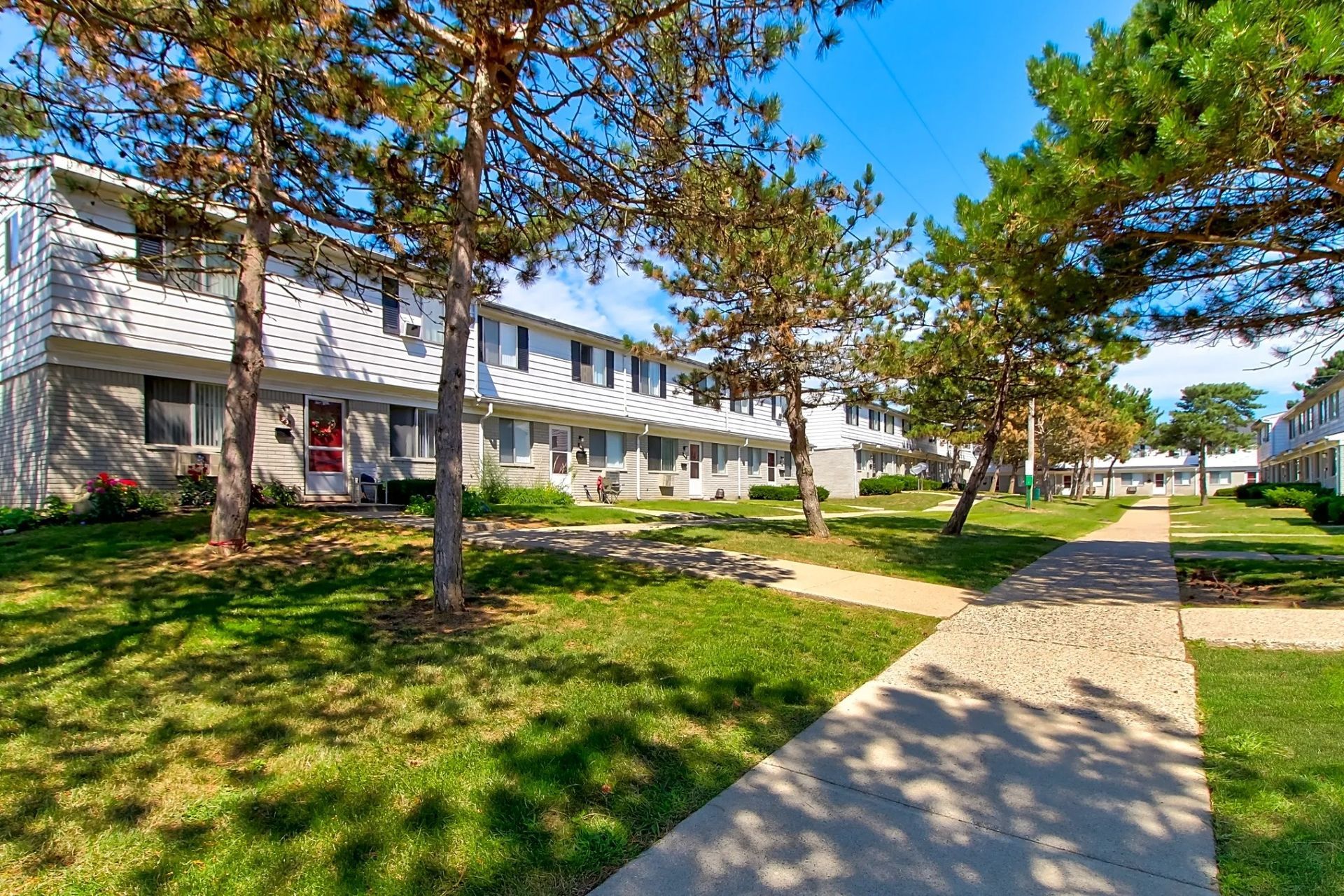 Apartment buildings and trees beside a sunny sidewalk in a landscaped courtyard
