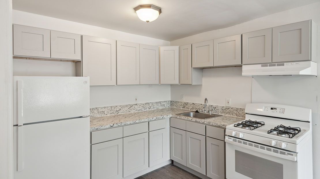 Bright white kitchen with cabinets, refrigerator, stove, and speckled countertop