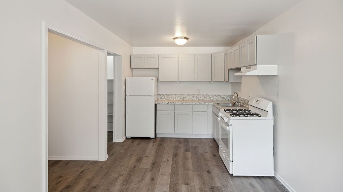 Bright white kitchen with white cabinets, stove, refrigerator, and wood-look flooring