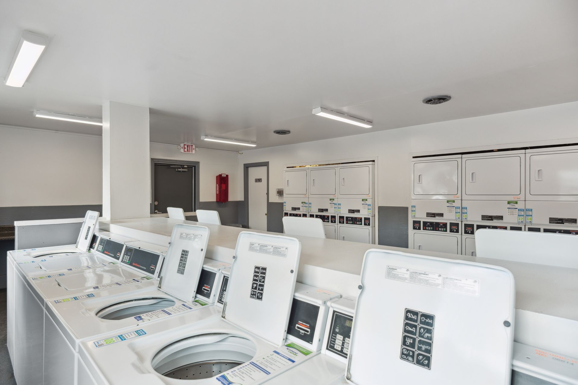 Bright laundromat interior with rows of white washing machines and dryers under fluorescent lights