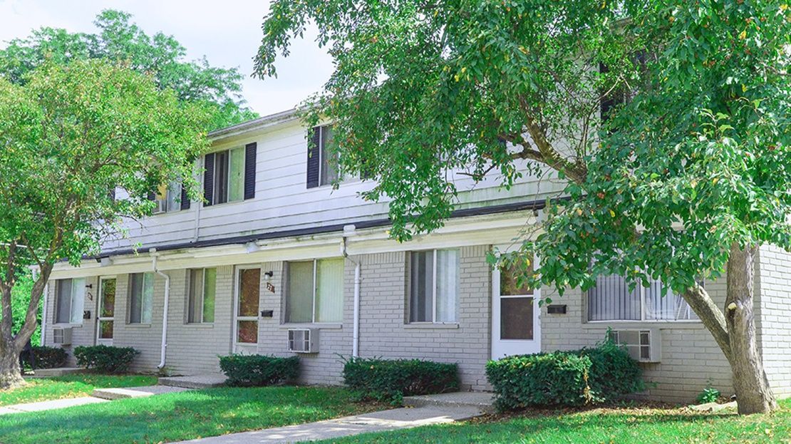 Two-story white house with dark shutters, a front porch, and trees shading the lawn