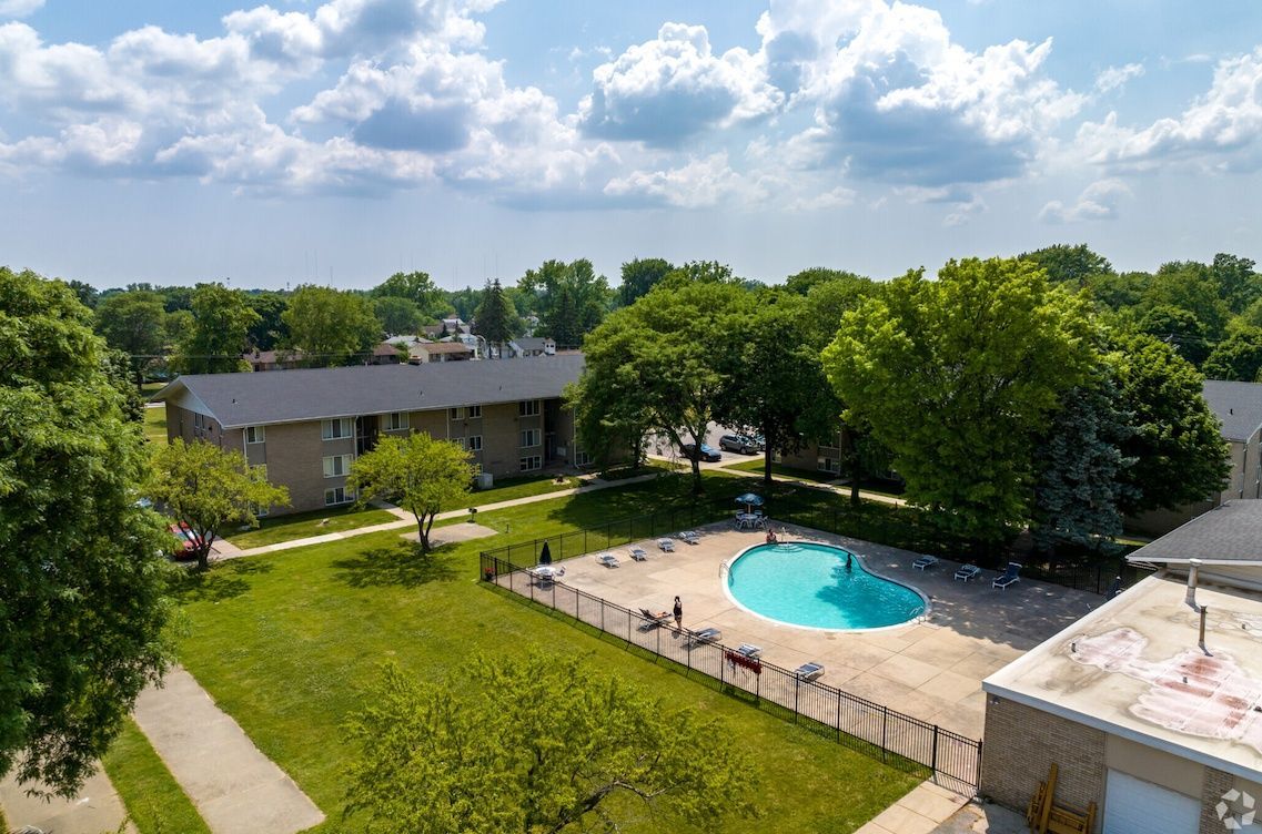 Aerial view of an apartment complex courtyard with a swimming pool, green lawn, trees, and patio seating.