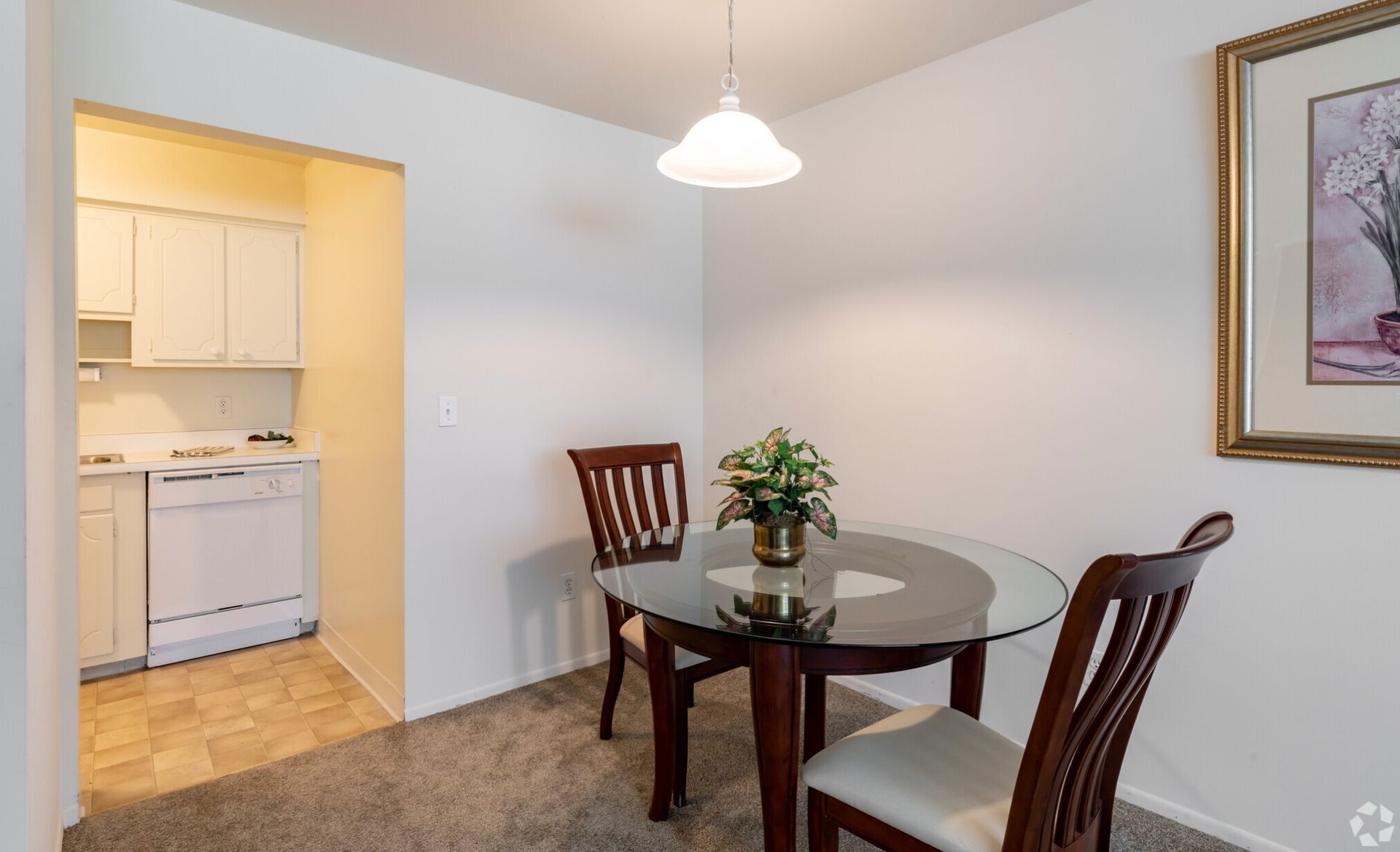 Small dining area with round glass table, wooden chairs, and a view into a kitchen.