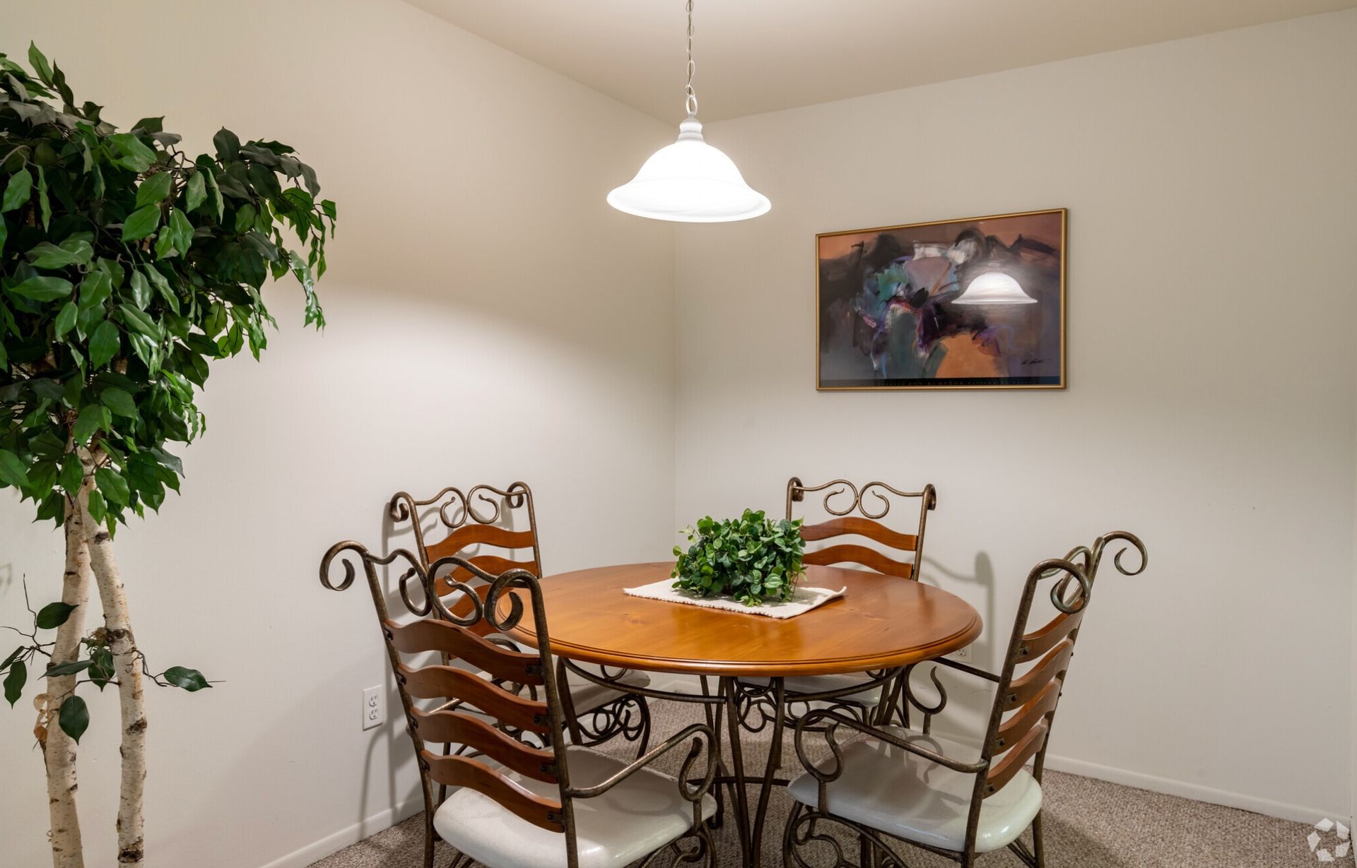 Dining nook with round wooden table, four chairs, hanging light, and wall art in a beige room
