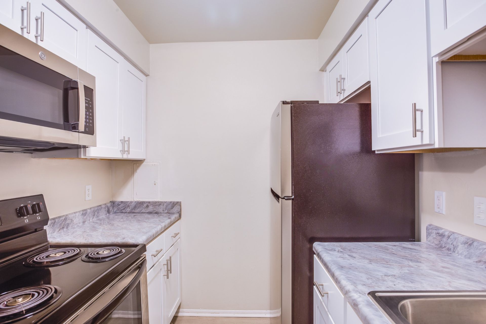 Small kitchen with white cabinets, stainless appliances, and speckled countertops