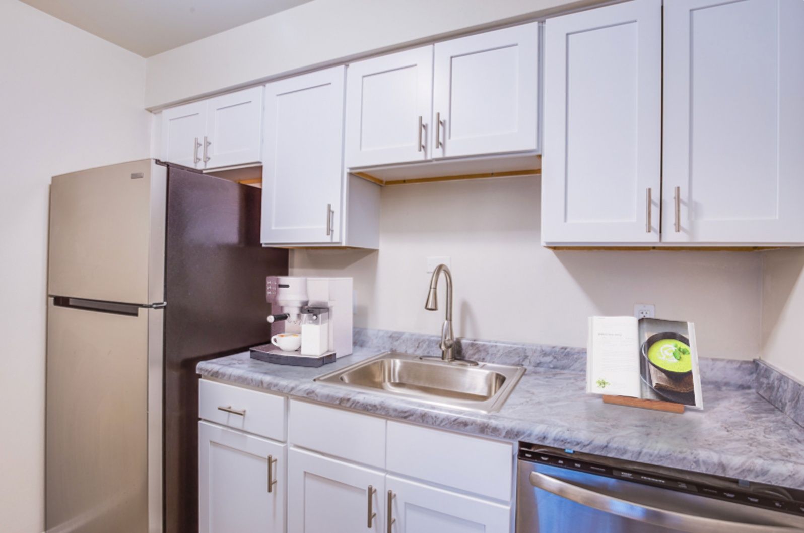 Small kitchen with white cabinets, gray countertops, stainless sink, and a refrigerator on the left.