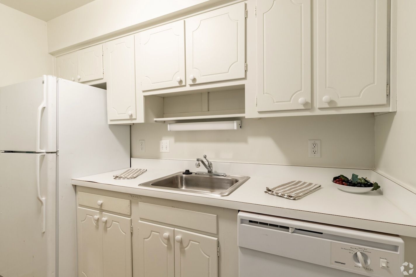 White kitchen with cabinets, sink, refrigerator, stove, and dishwasher along a long countertop.