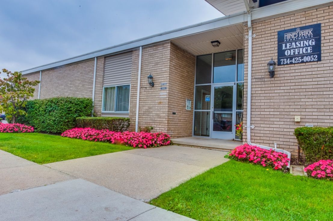 Entrance to a brick office building with glass doors, blue sign, and pink flowers along the walkway