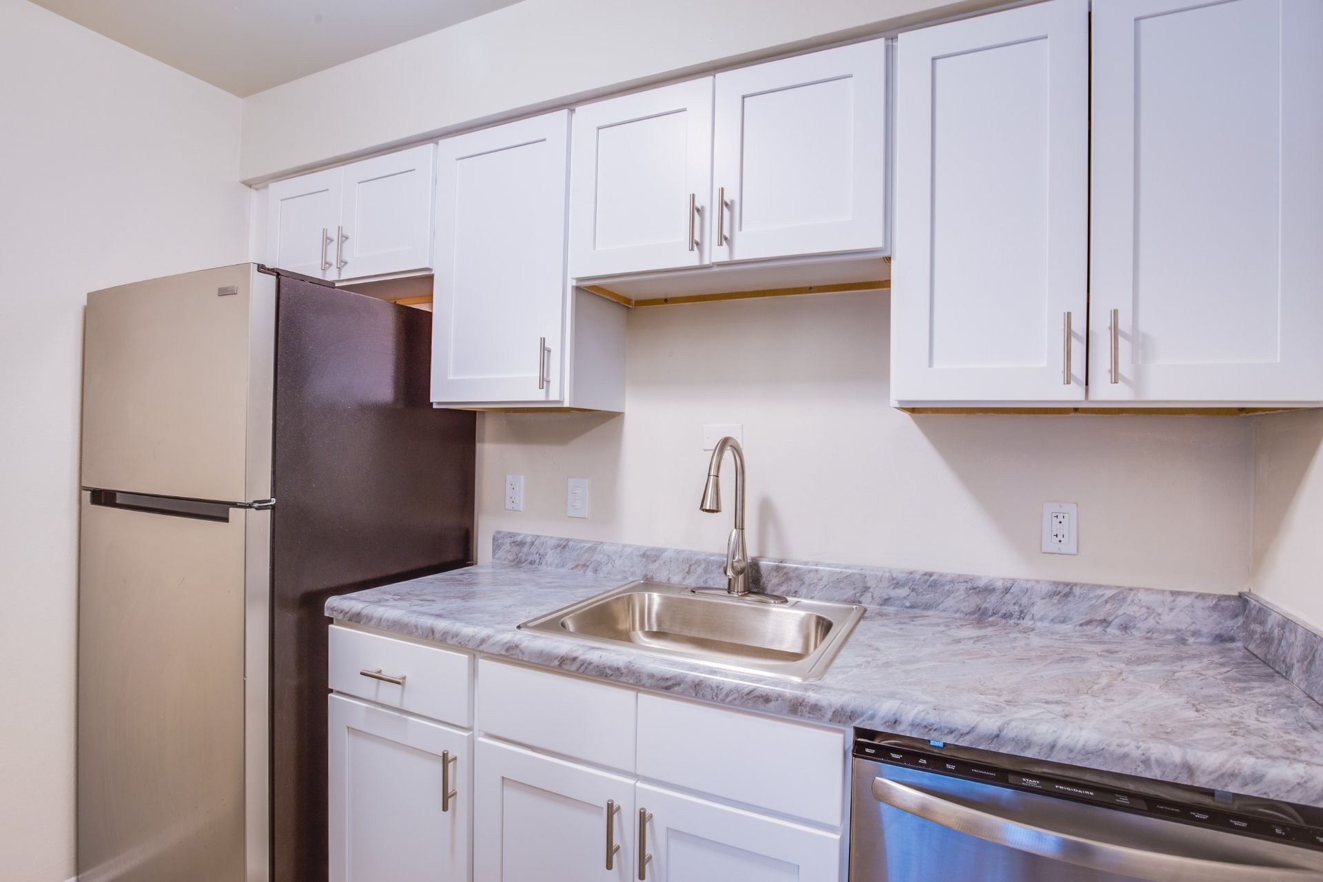 Compact kitchen with white cabinets, stainless fridge and sink, and gray marbled countertops