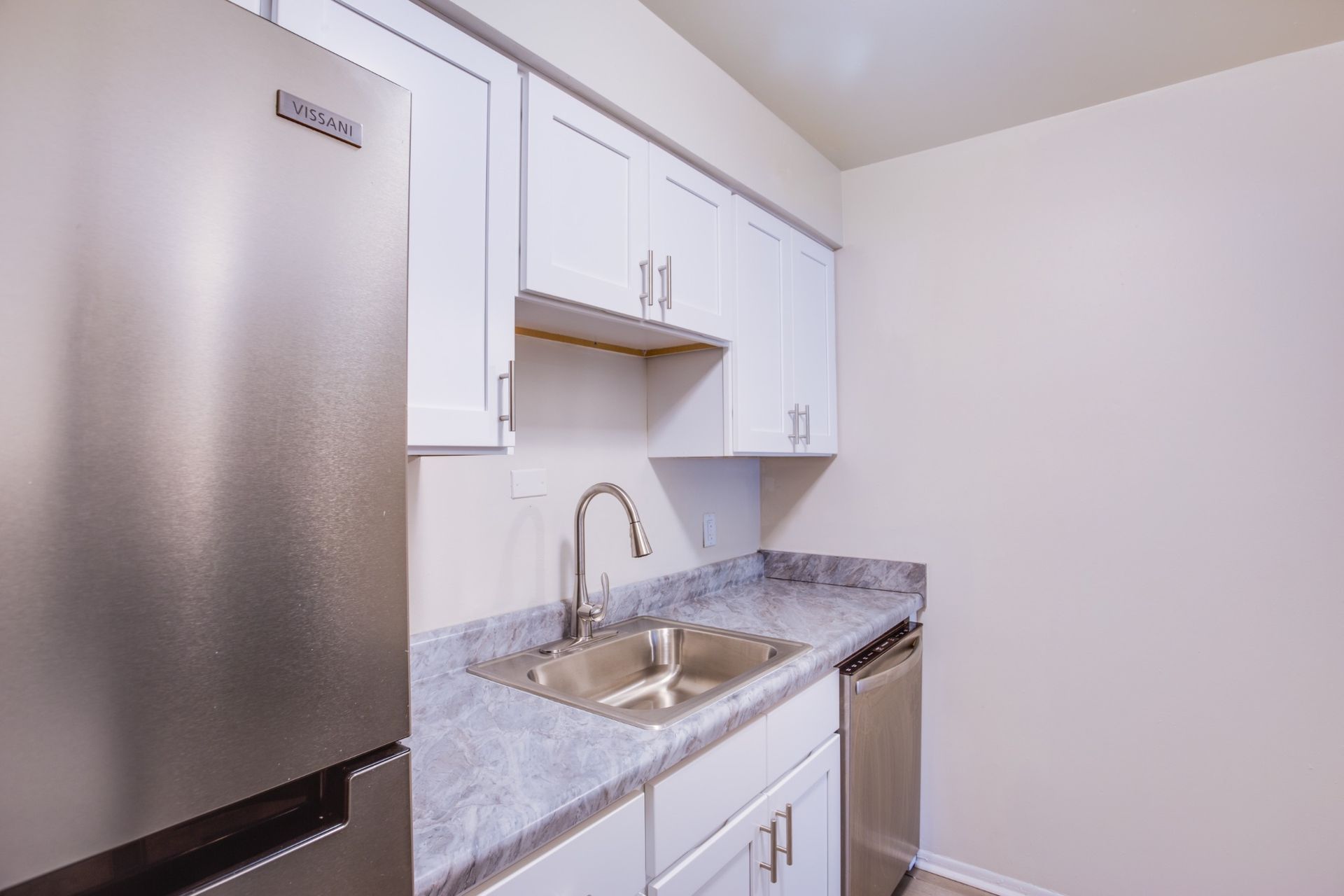 Small kitchen with stainless steel fridge, white cabinets, and granite countertop with sink.