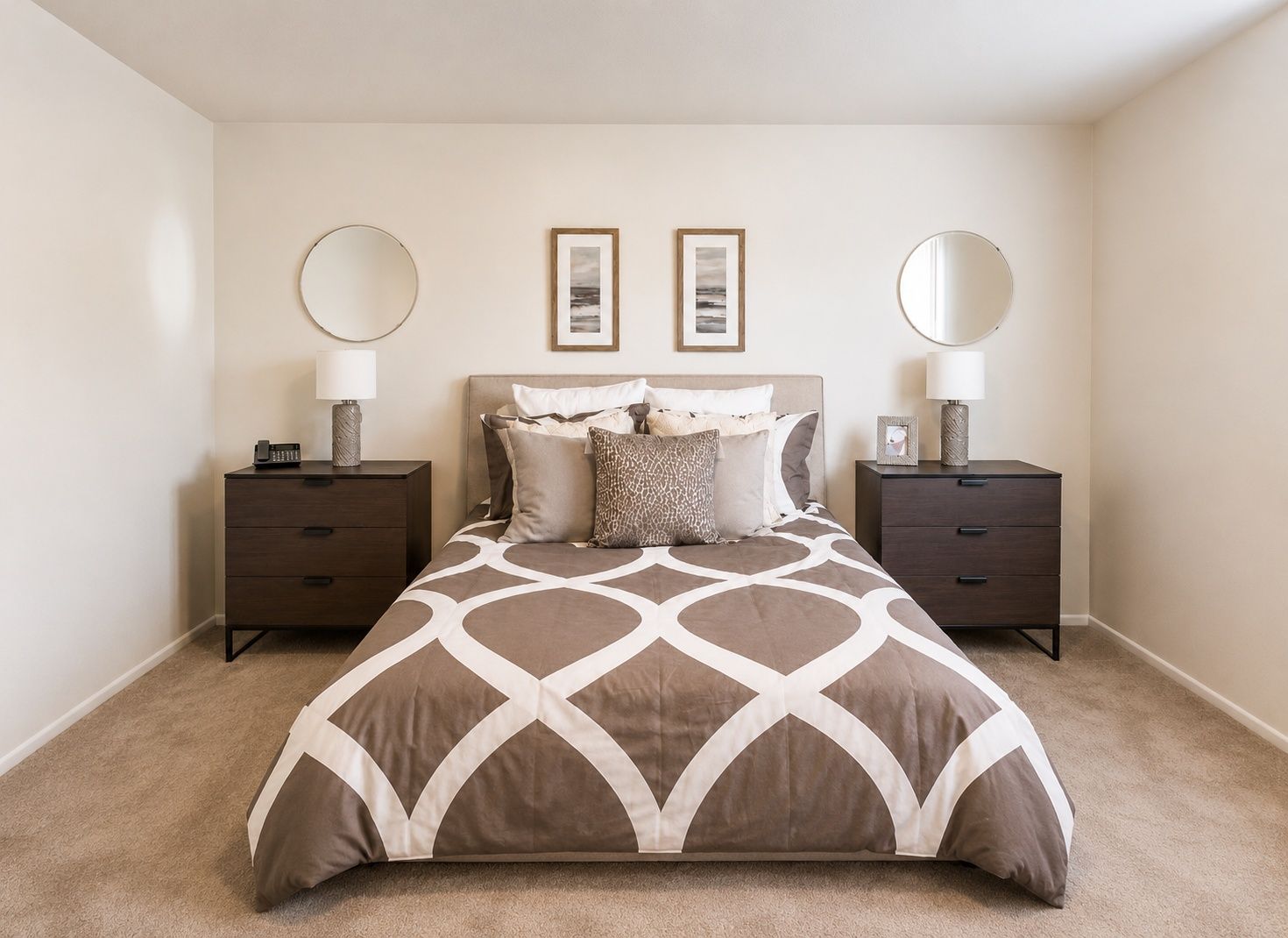Neatly made bedroom with a patterned bed, two dark nightstands, and framed art above the headboard