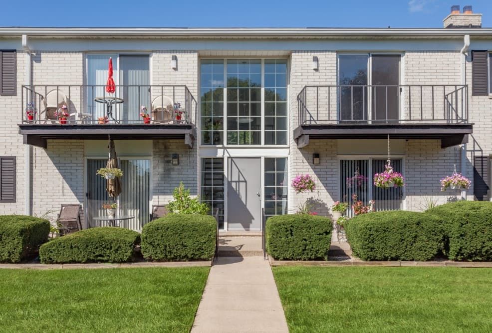 Apartment building with balconies, hanging flowers, and a central walkway across a green lawn