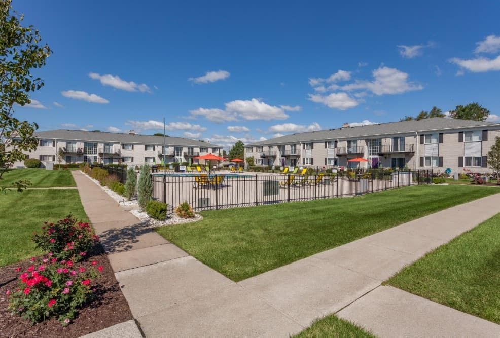 Apartment complex courtyard with walkways, lawns, flower beds, and a blue sky.