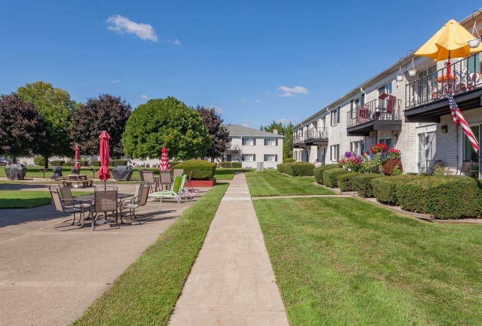 Apartment courtyard with central walkway, patio tables, umbrellas, and balconies on a sunny day