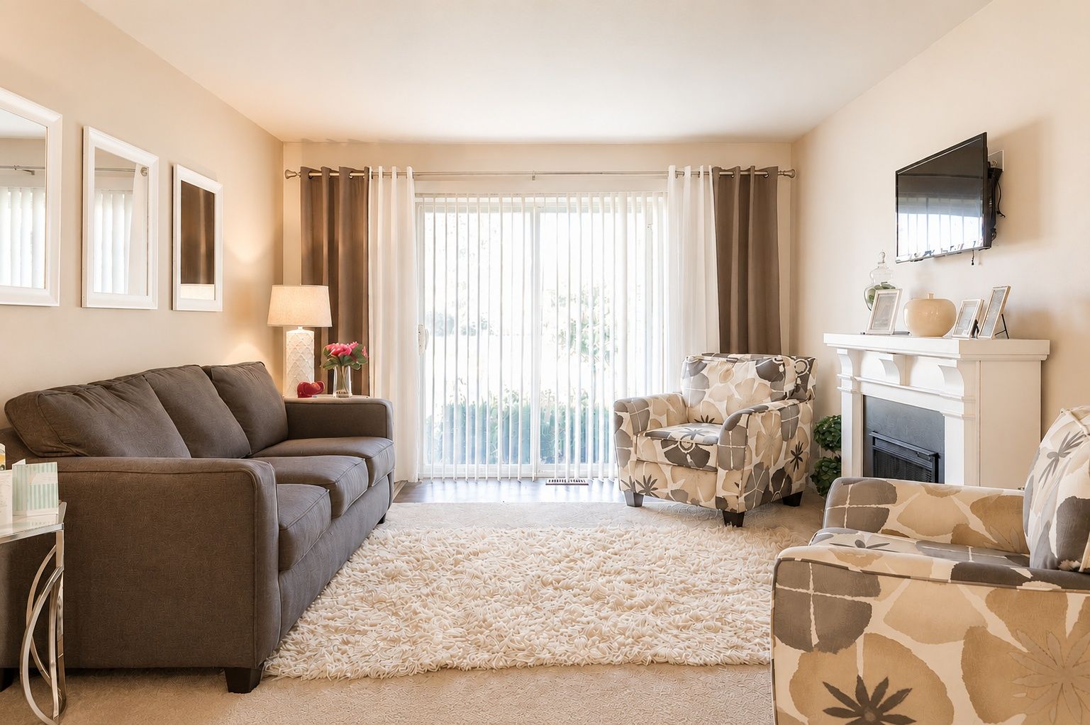 Bright living room with gray sofa, fireplace, armchair, and sliding glass doors with sheer curtains.