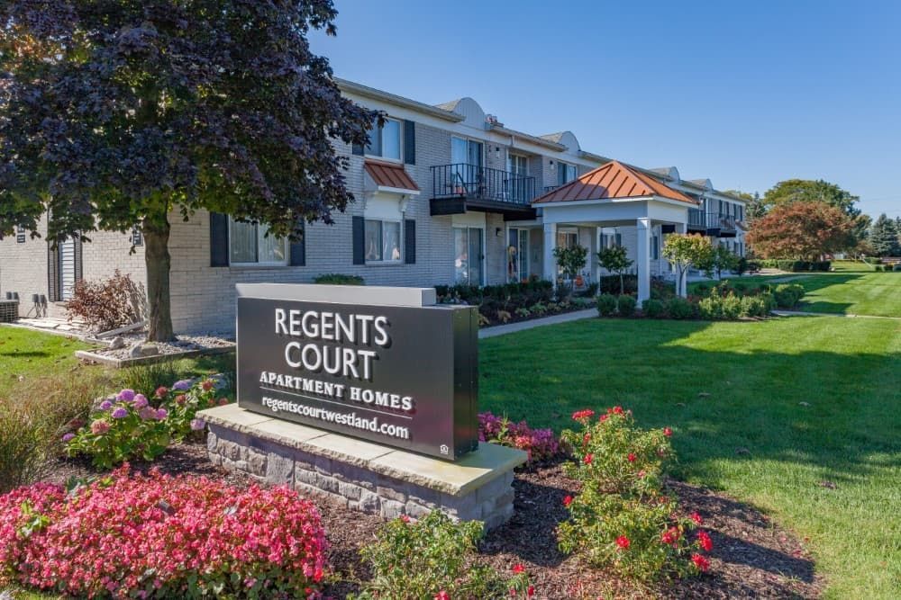 Regents Court apartment homes sign beside landscaped lawn and white residential buildings on a sunny day