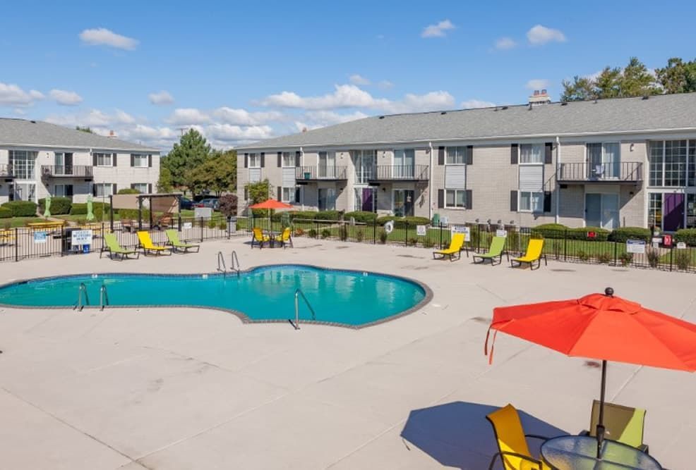 Apartment complex pool with lounge chairs and red umbrellas on a sunny day