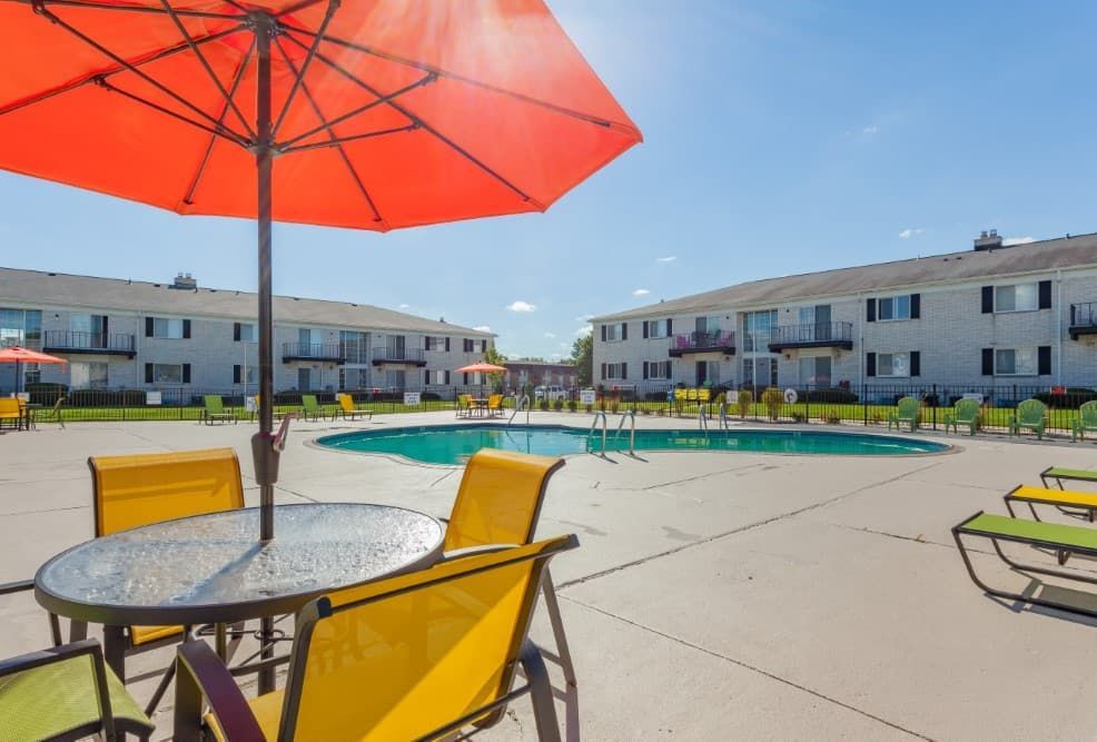 Courtyard with pool, red umbrella, and yellow chairs outside apartment buildings