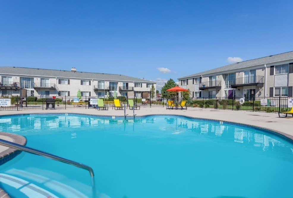 Outdoor apartment pool with blue water, lounge chairs, and colorful umbrellas under a clear sky