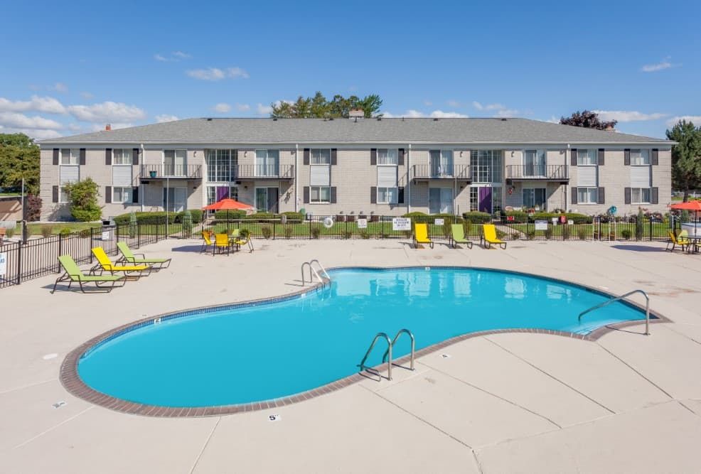 Apartment pool with blue water, lounge chairs, and a two-story building in the background