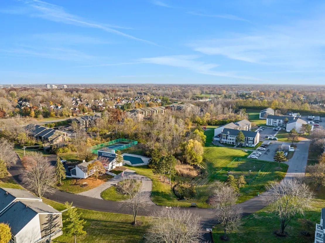 Aerial view of a suburban neighborhood with houses, trees, roads, and a clear blue sky