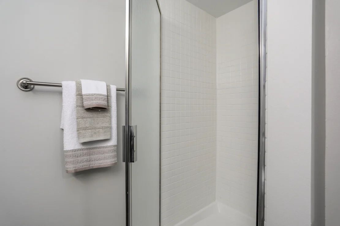 White bathroom towel hanging on a metal rack beside a shower stall.