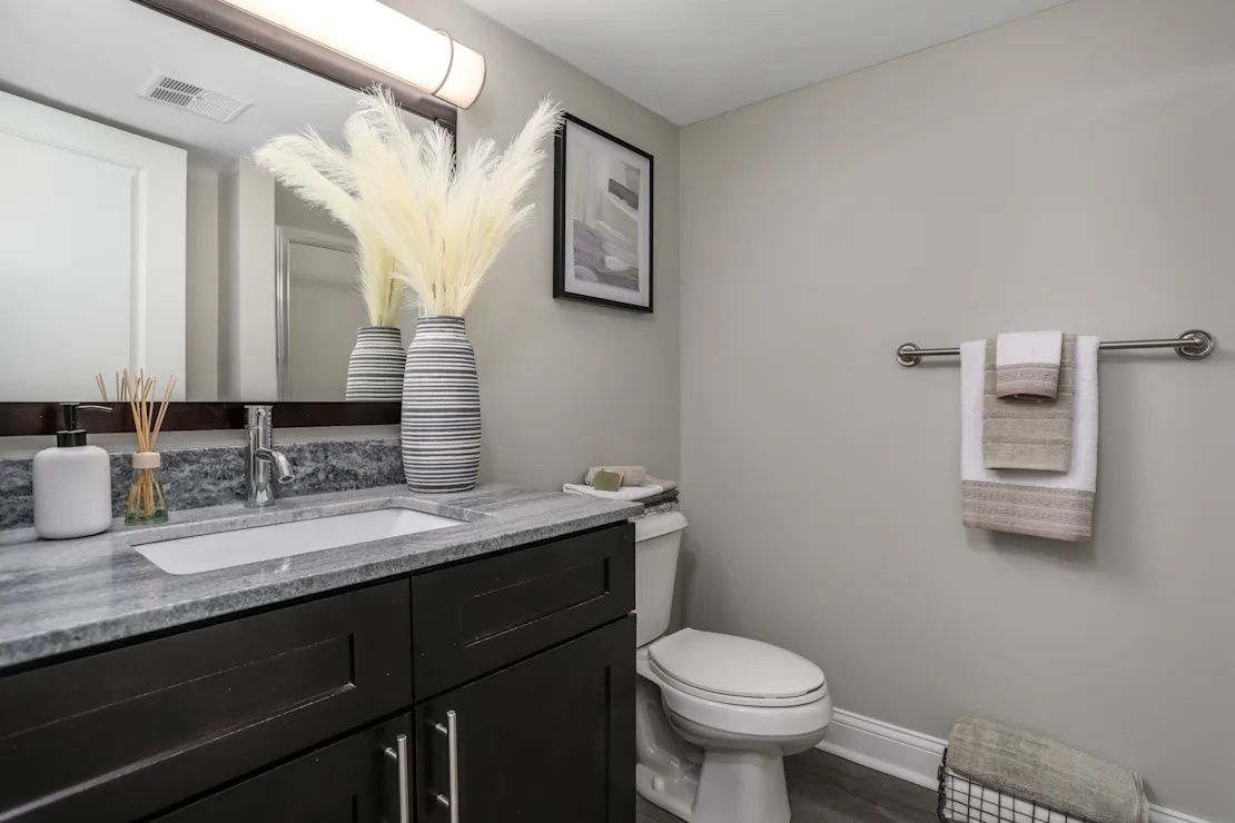 Modern bathroom with dark vanity, marble countertop, toilet, and white towel rack