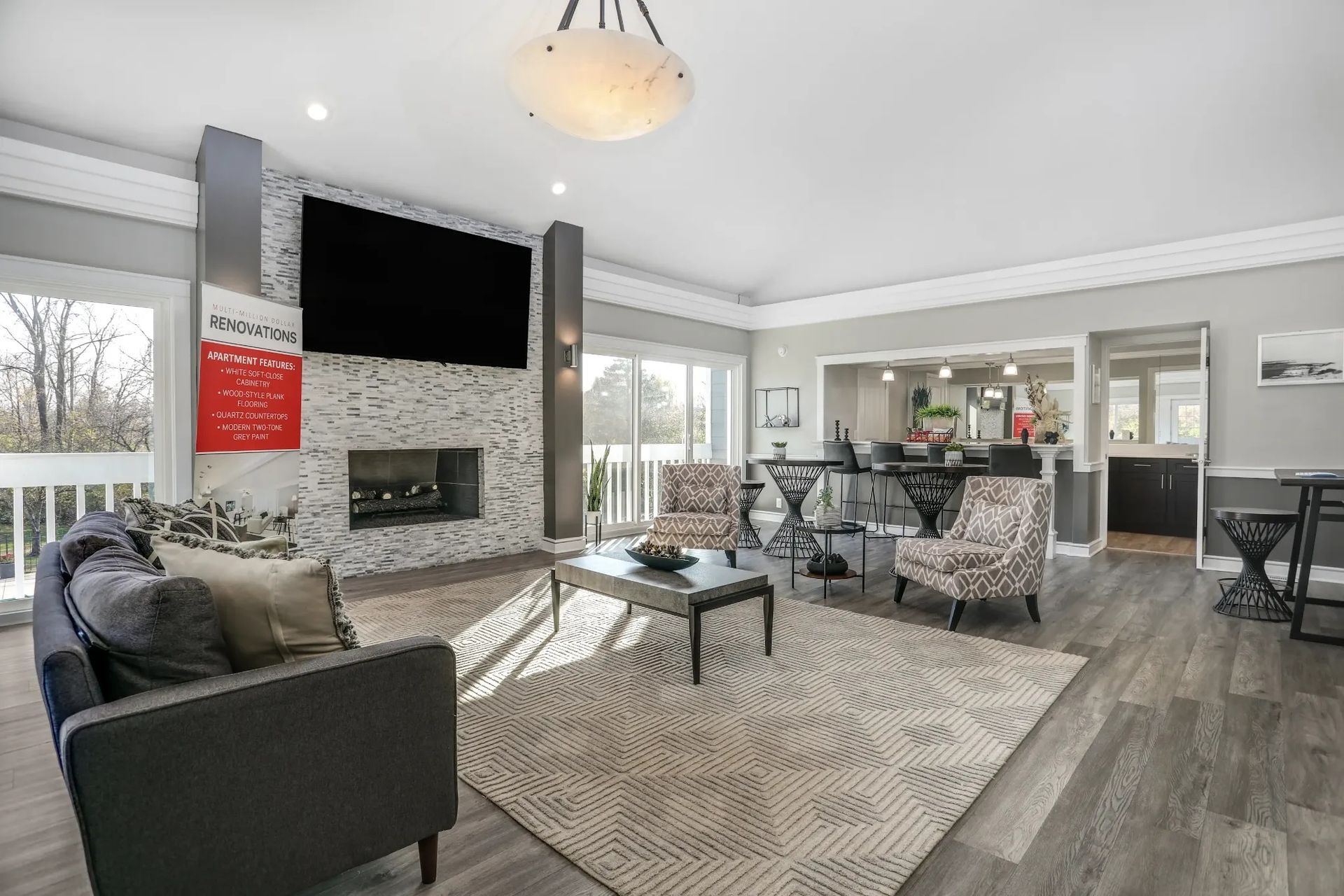 Modern living room with gray sectional, stone fireplace, patterned rug, and open view to dining and kitchen area