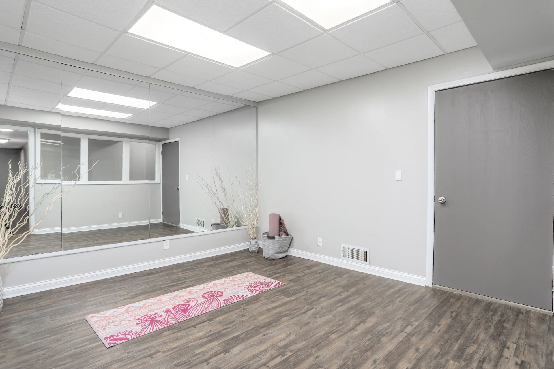 Empty modern office lobby with wood floor, white walls, gray door, and a pink rug near a raised platform.