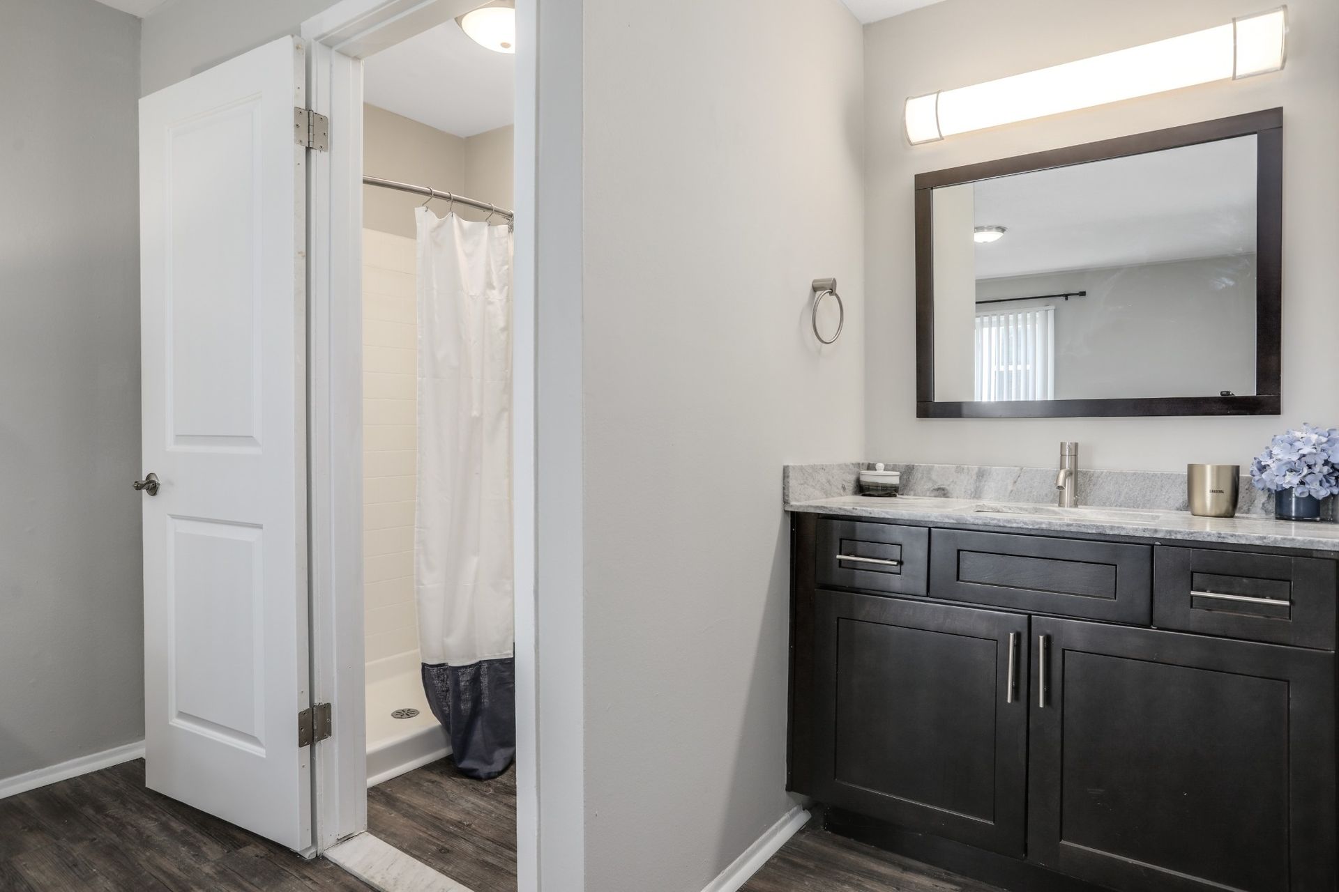 Bathroom vanity and mirror beside an open door to a shower with white curtain