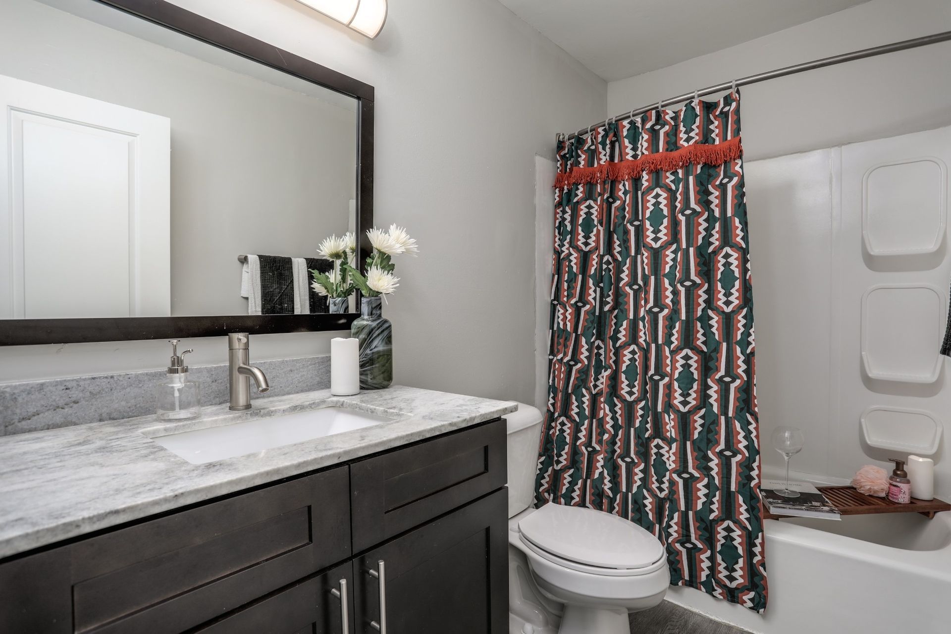Modern bathroom with dark vanity, marble countertop, toilet, bathtub, and patterned shower curtain