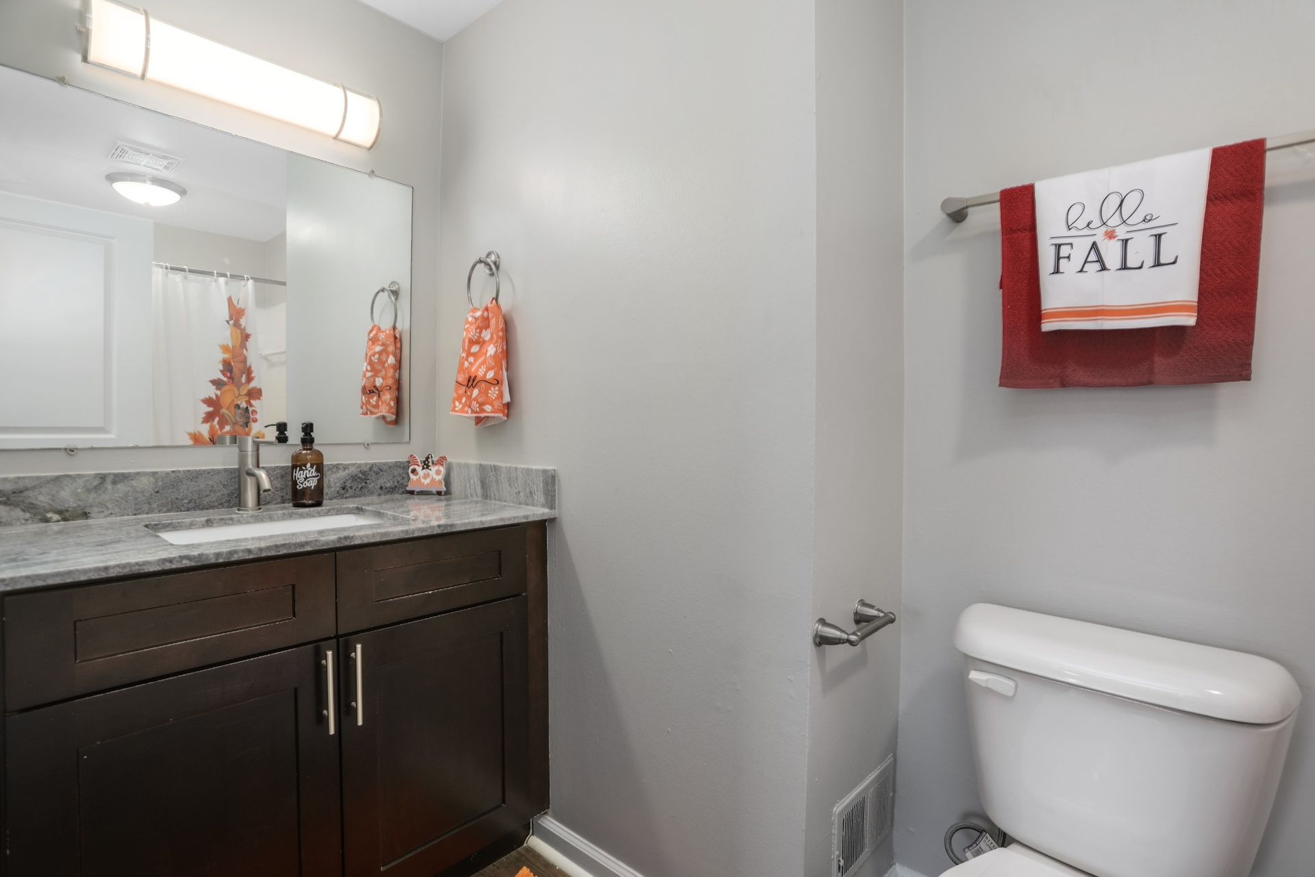 Small bathroom with dark vanity, sink, toilet, and red “Fall” wall decor.