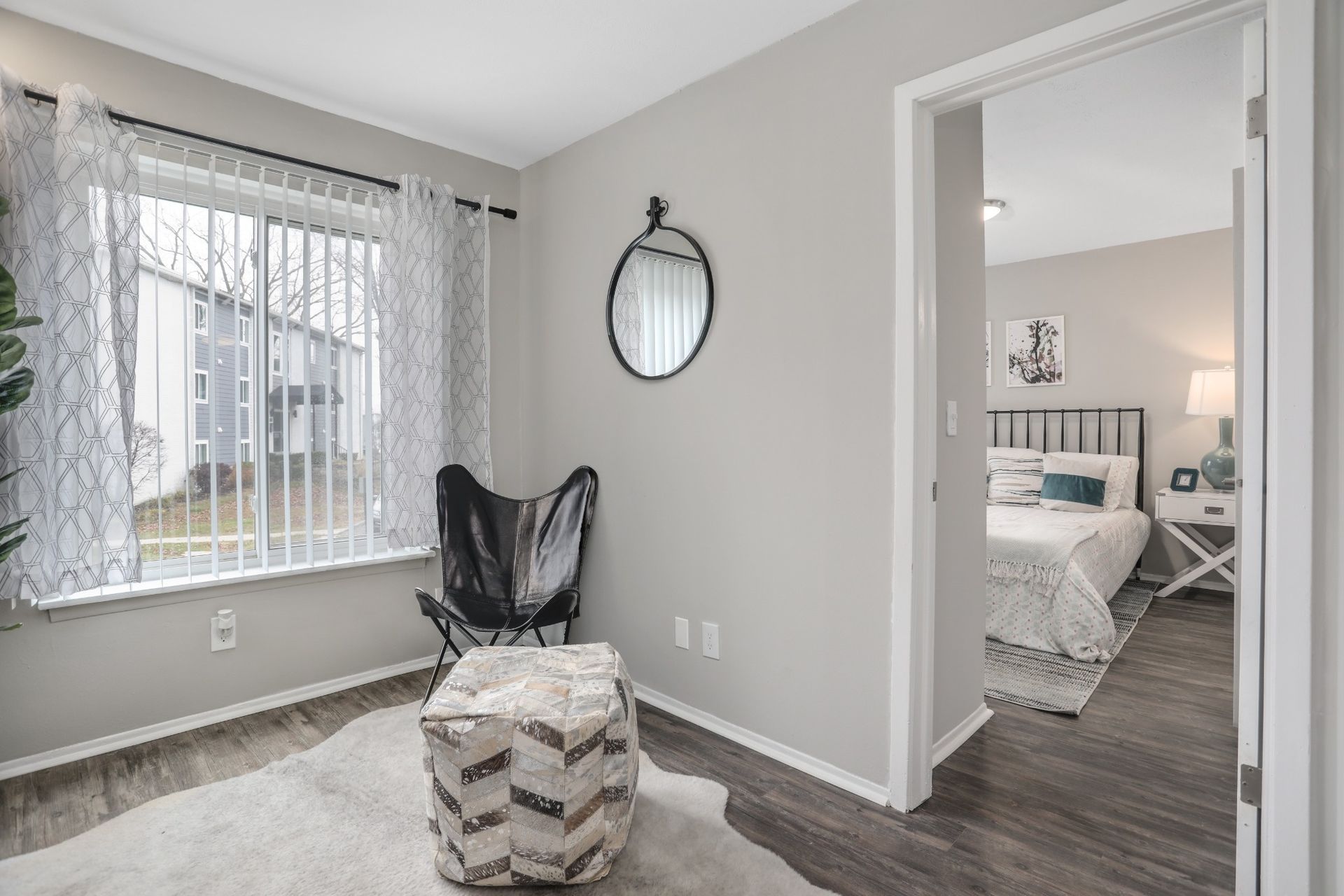 Bright gray bedroom with window bench, black chair, wall mirror, and adjoining bed alcove