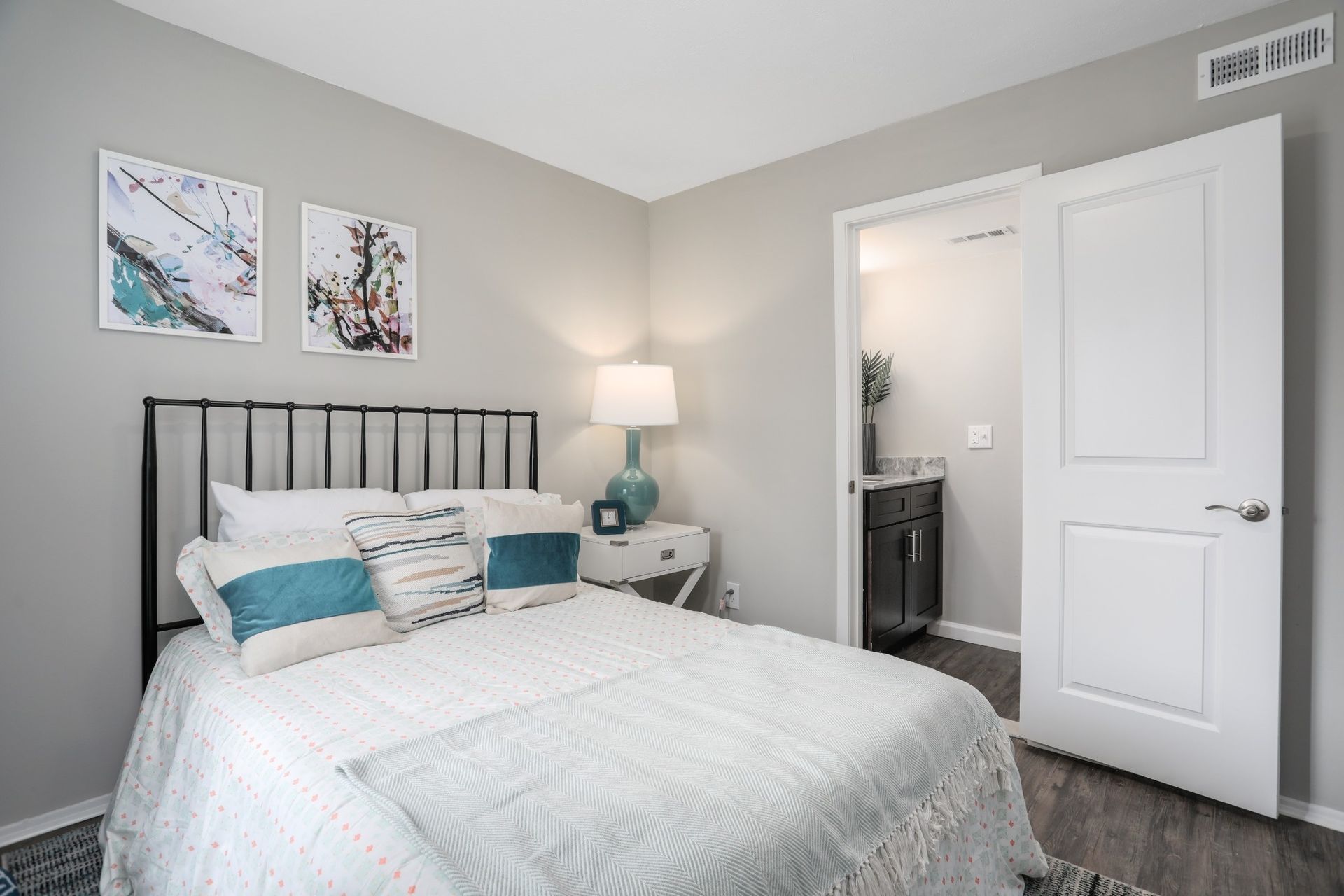 Bright bedroom with a bed, teal accents, bedside lamp, and open door to a bathroom