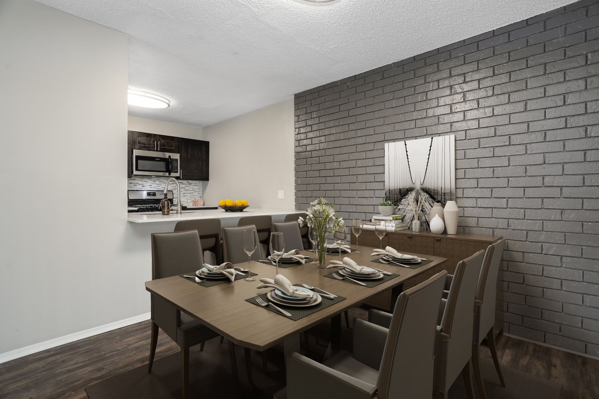 Dining room with a set table, gray chairs, and a gray brick accent wall next to a kitchen pass-through