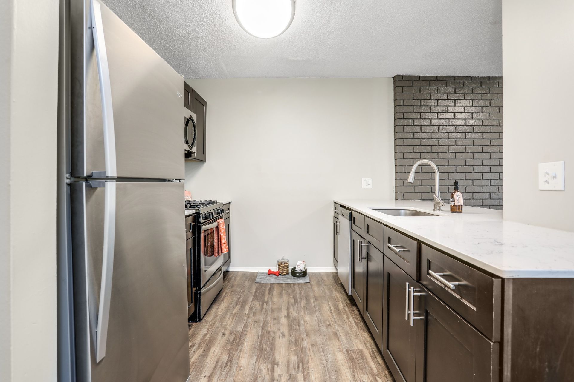 Modern kitchen with stainless steel fridge, dark cabinets, white countertop, and brick-style backsplash.