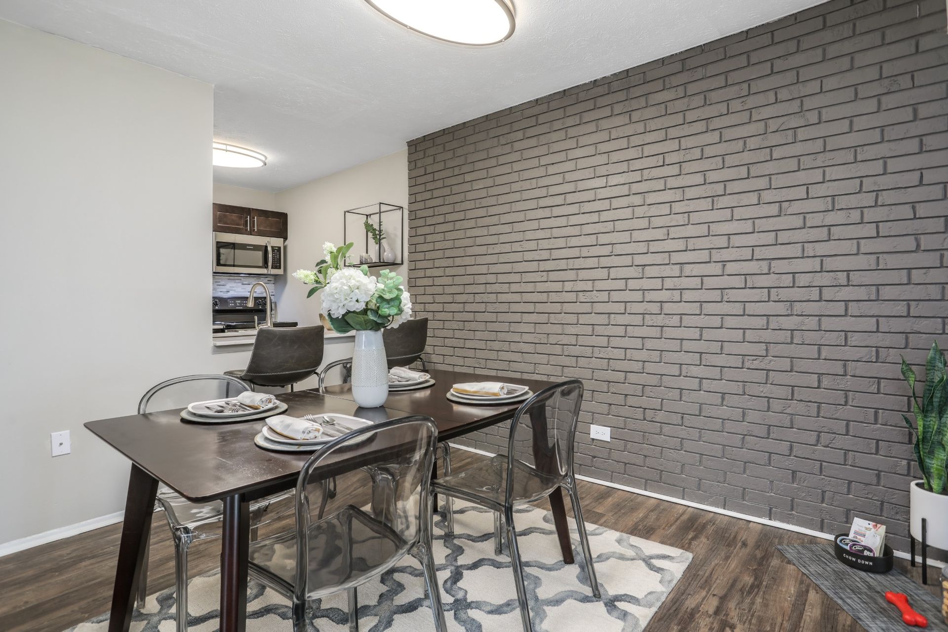 Dining area with a dark wood table, chairs, a flower centerpiece, and a gray brick accent wall.