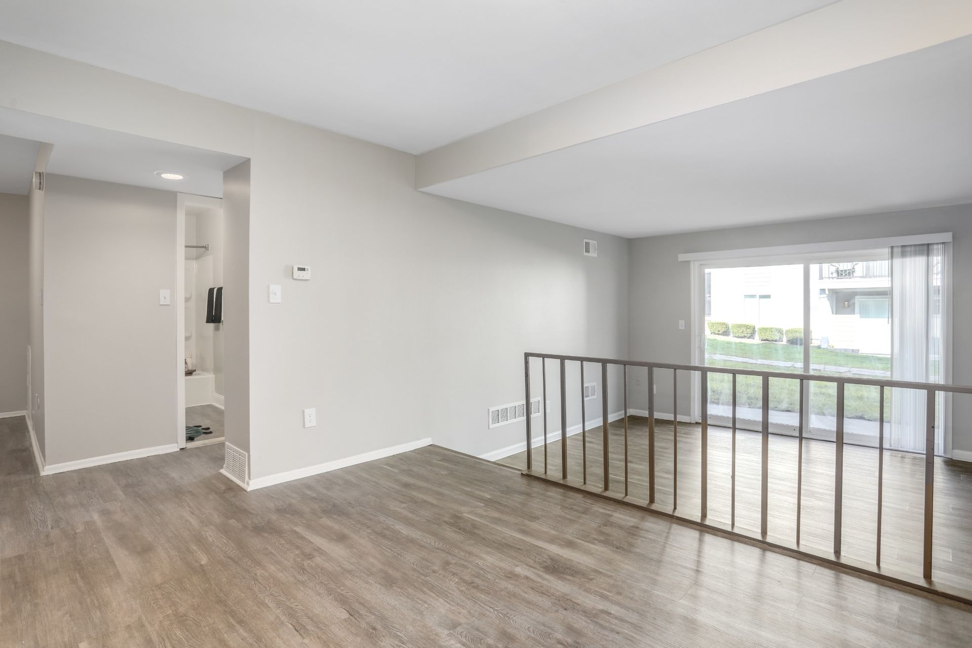 Empty modern living room with gray flooring, white walls, and large sliding glass doors to a balcony.