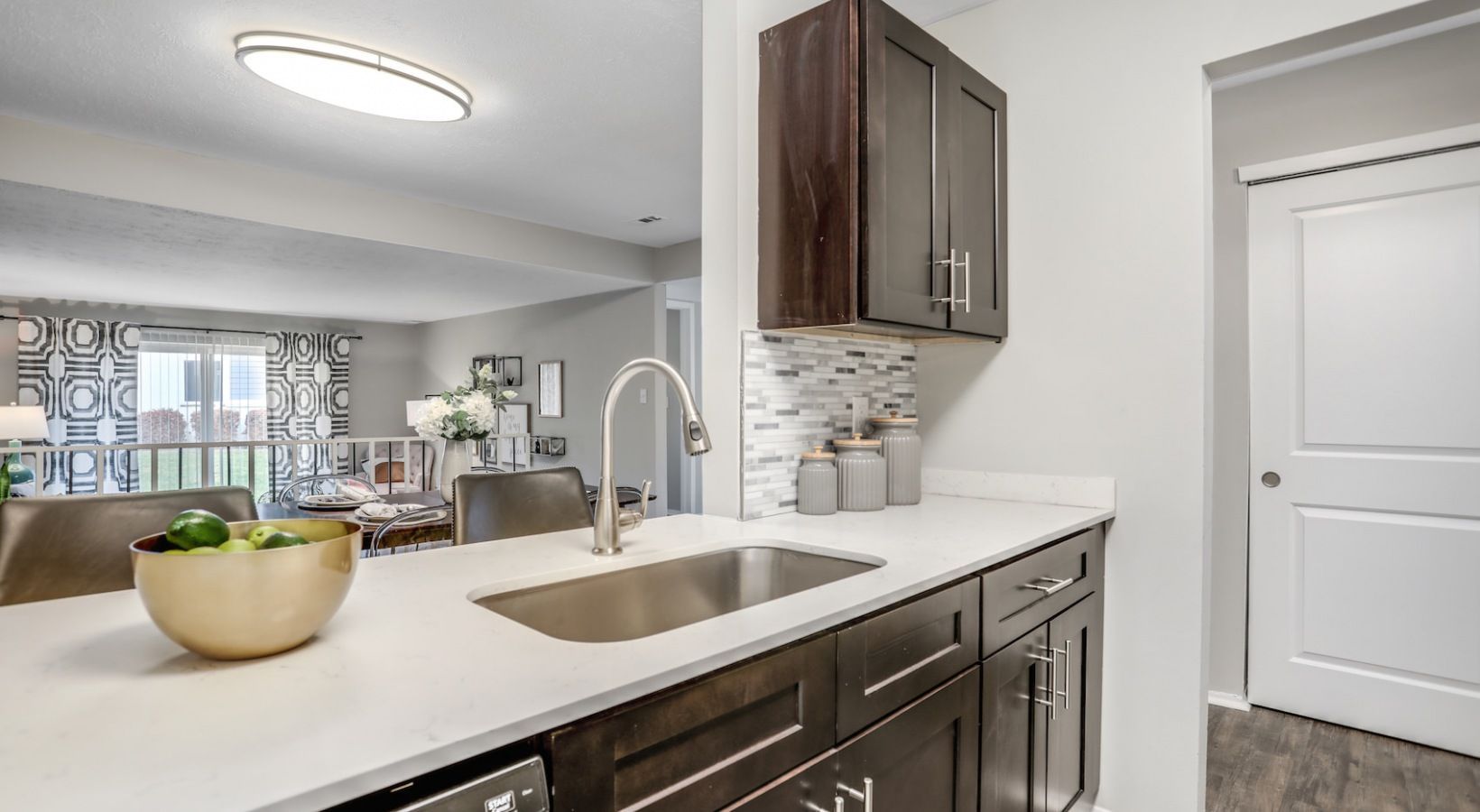Modern kitchen with white countertops, dark cabinets, sink, and a view into a bright living room
