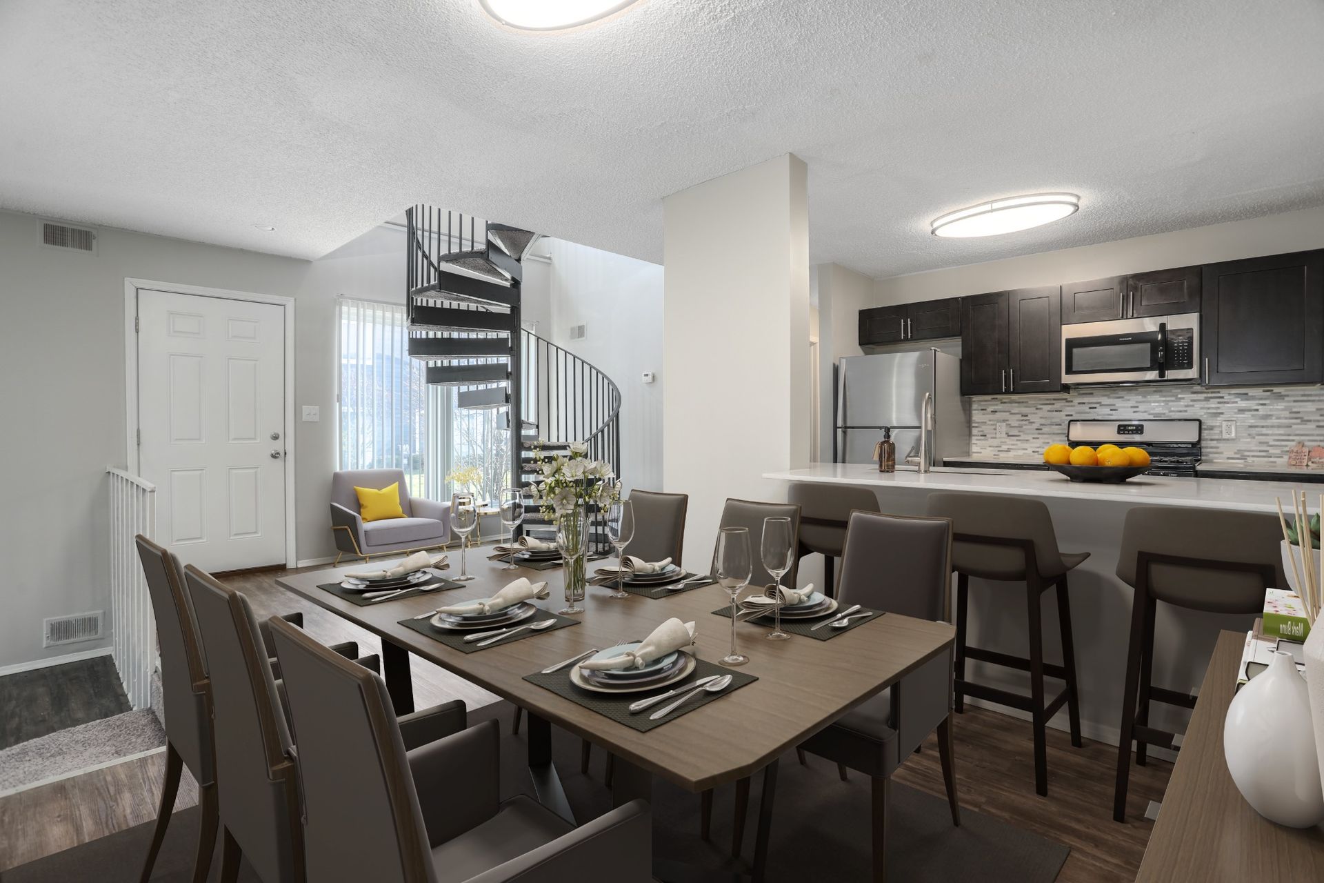 Modern apartment dining area with set table, spiral staircase, and open kitchen with bar stools.