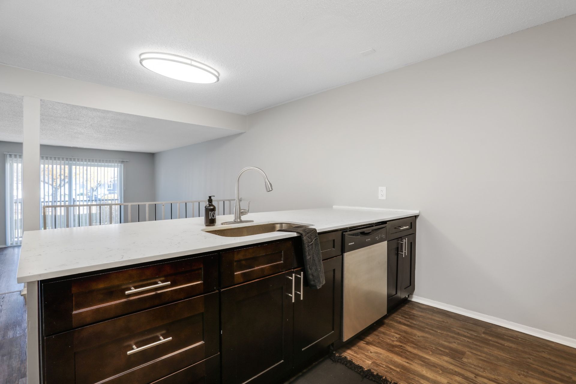 Modern kitchen with white countertops, dark wood cabinets, and stainless steel appliances under bright ceiling light