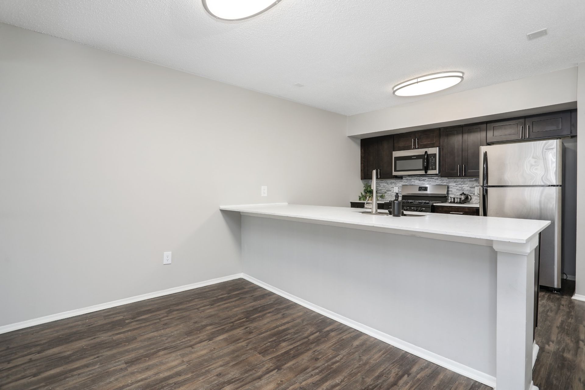 Empty kitchen with white breakfast bar, dark wood flooring, and stainless steel appliances in the background