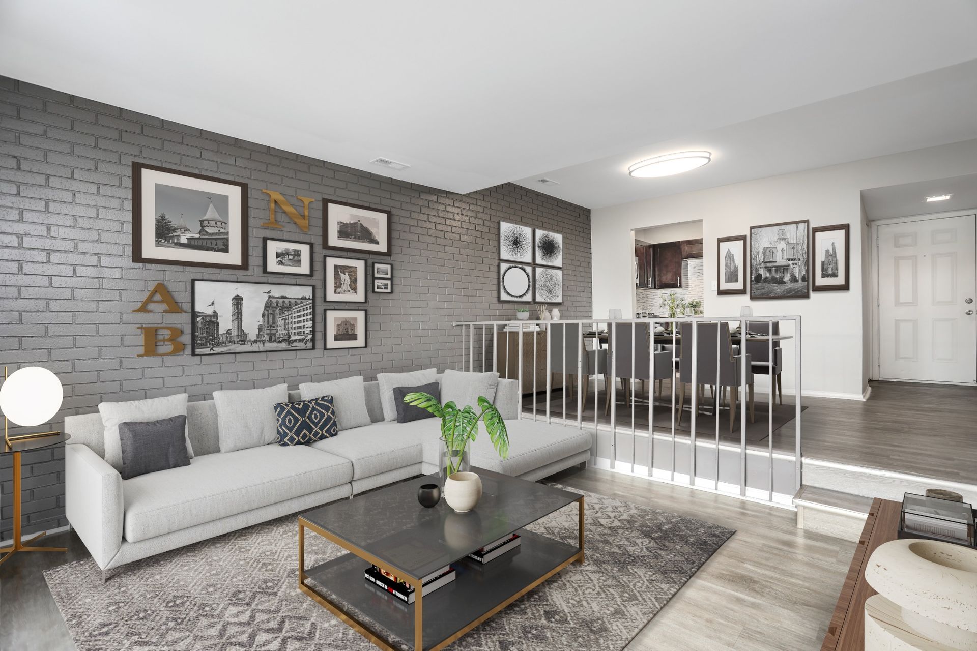 Modern gray living room with sofa, coffee table, wall art, and stair railing leading to dining area