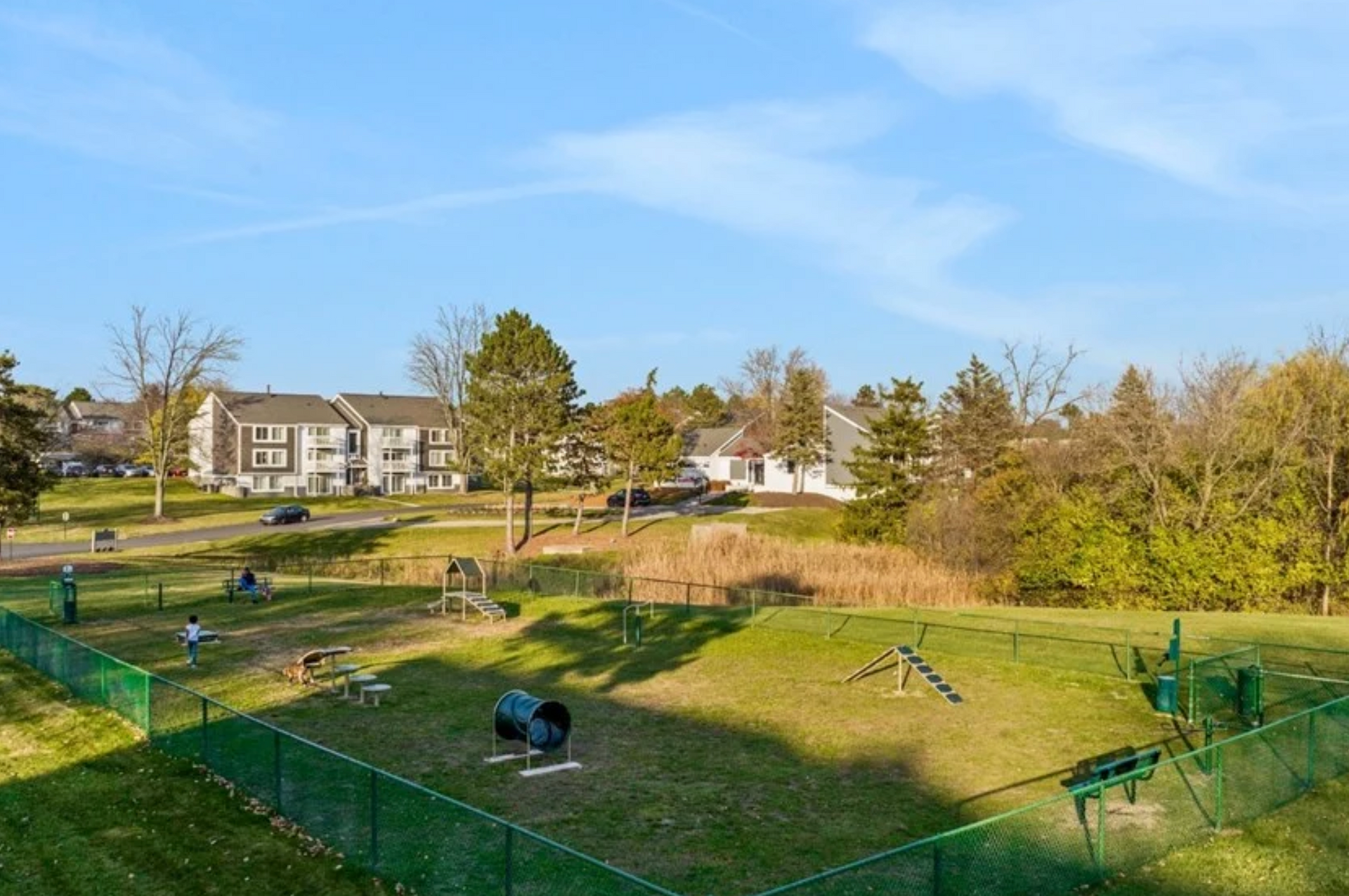 Sunlit park with grassy hills, fenced play area, and apartment buildings in the background
