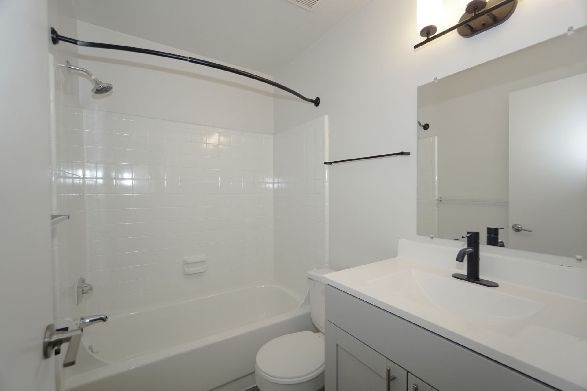 Bright white bathroom with tub, glass shower door, vanity sink, and mirror