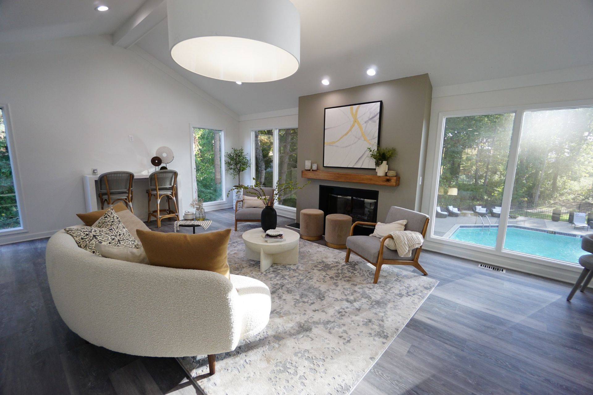 Bright modern living room with curved sofa, fireplace, large windows, and pool view