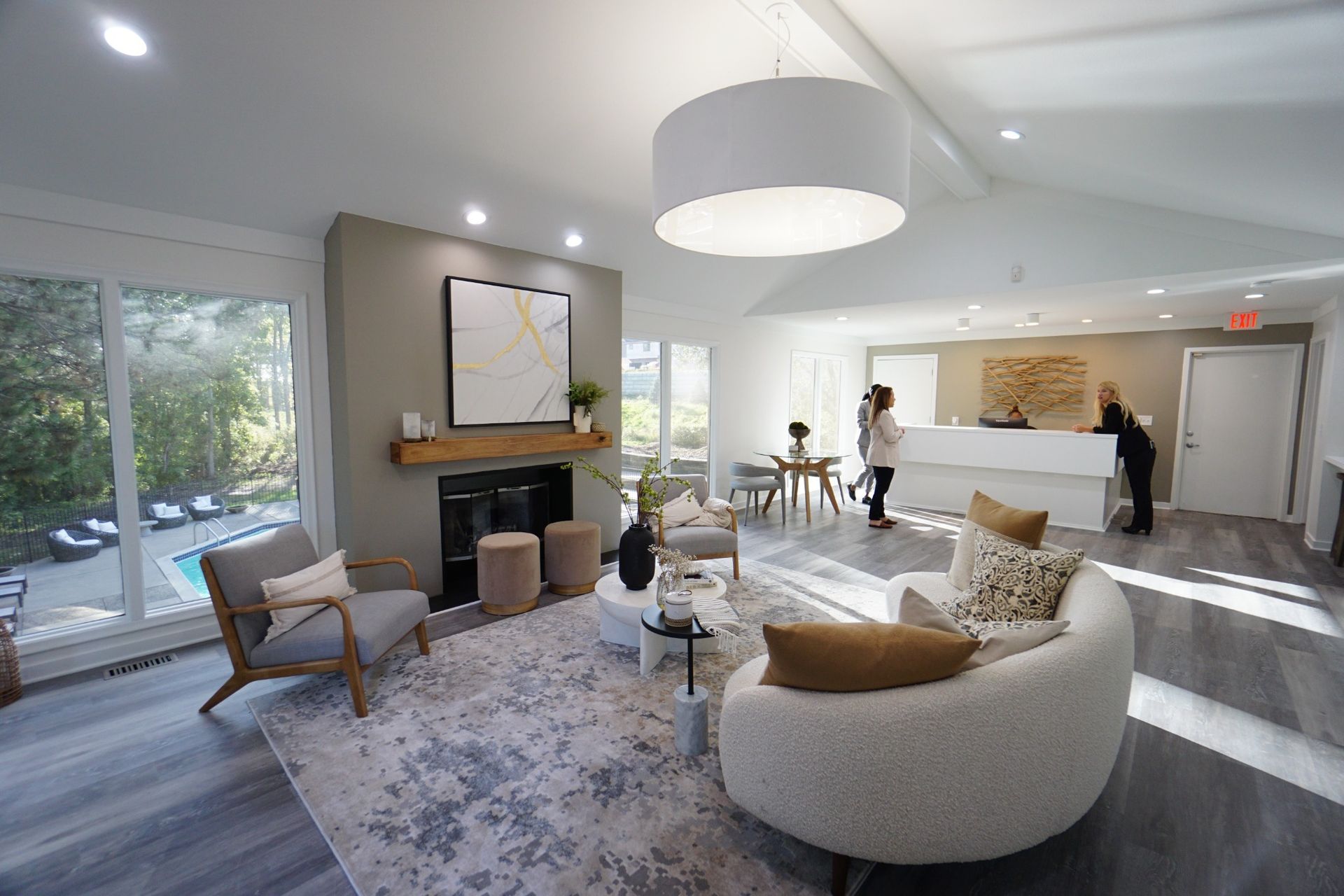 Modern living room with gray sofa, fireplace, large windows, and a person standing by the counter