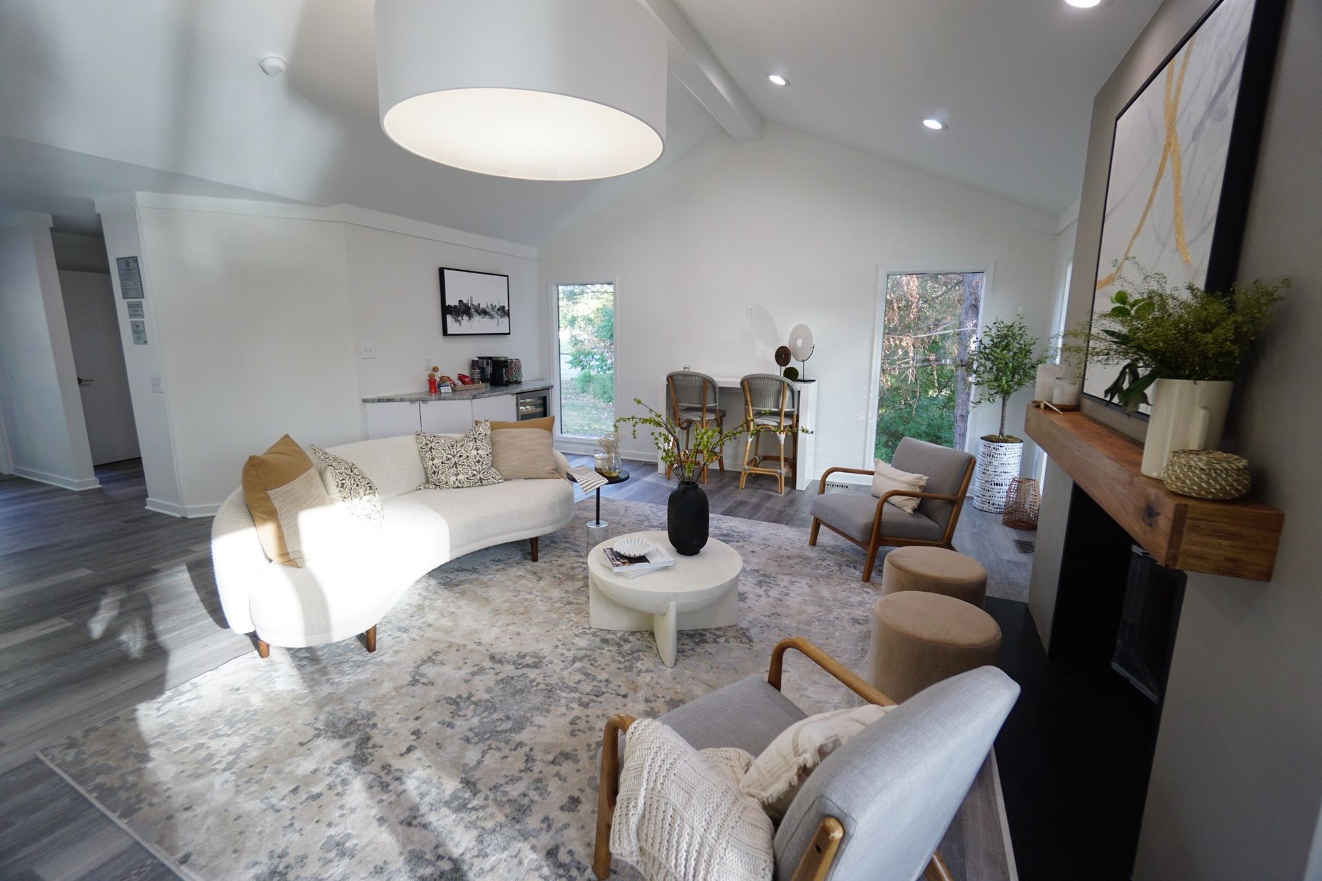 Modern living room with white chairs, round coffee table, fireplace, and large windows
