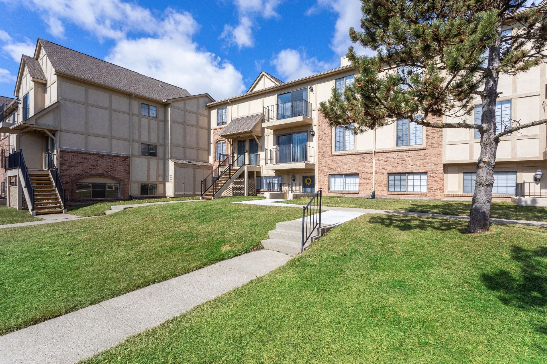 Apartment complex courtyard with green lawn, sidewalks, and blue sky